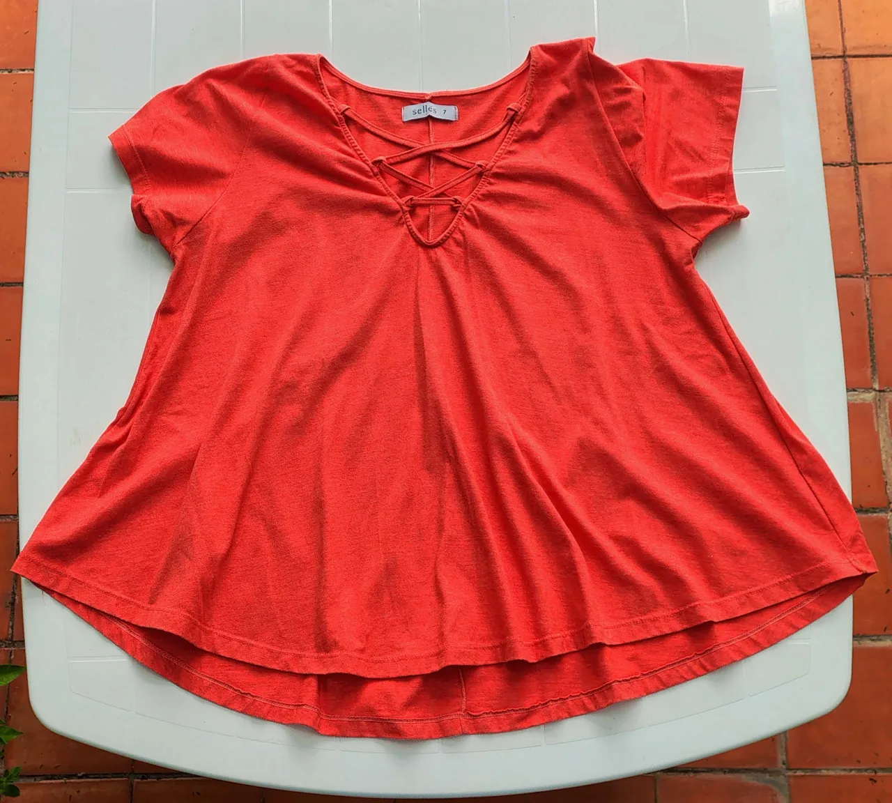 Remera de color naranja con escote en V y cordones cruzados. Posee mangas cortas y es de tela liviana.