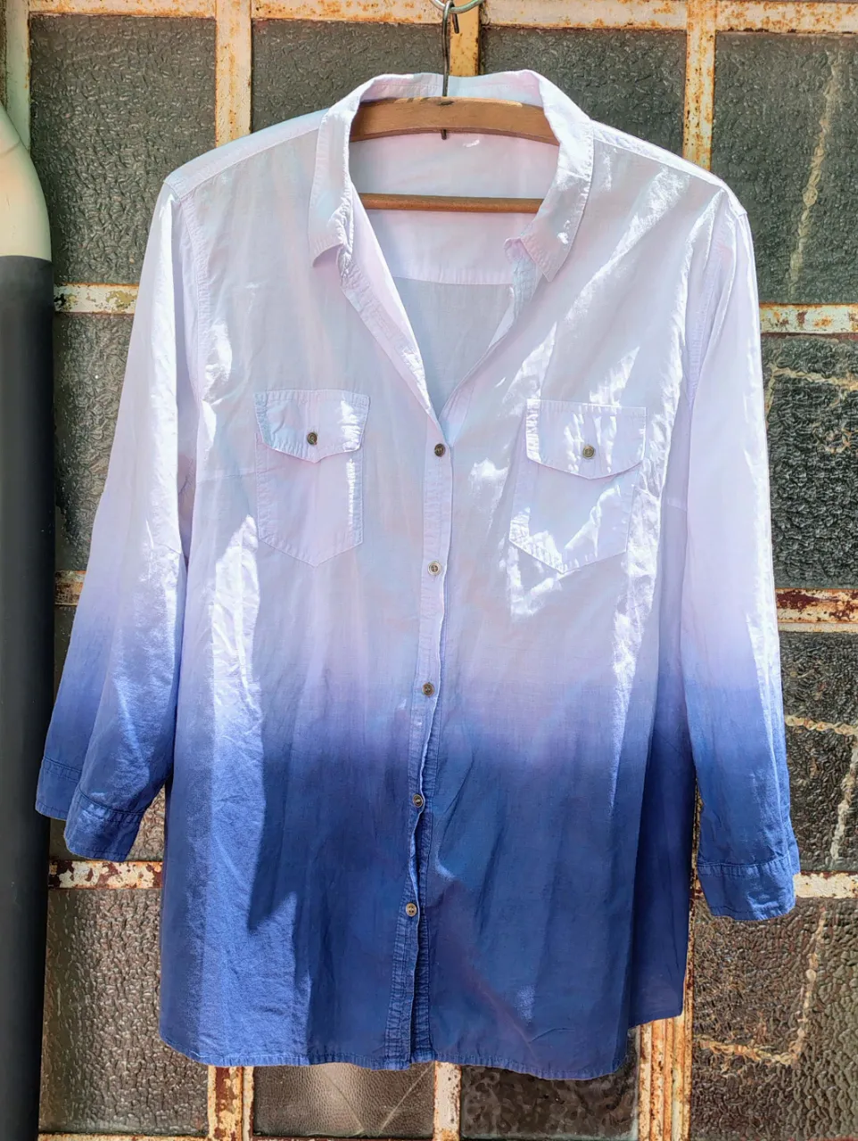 Camisa con degradado de color blanco a azul. Posee dos bolsillos en el frente y botones en la parte central y en los puños.