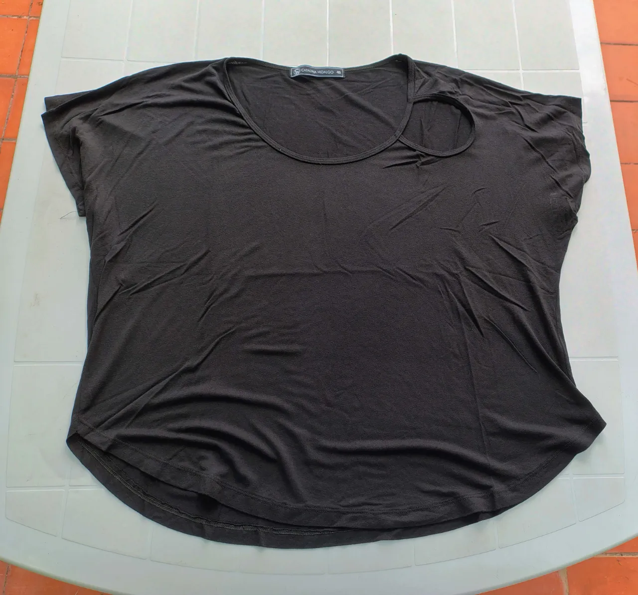 Remera negra de manga corta con escote redondo y un recorte circular en el hombro izquierdo.