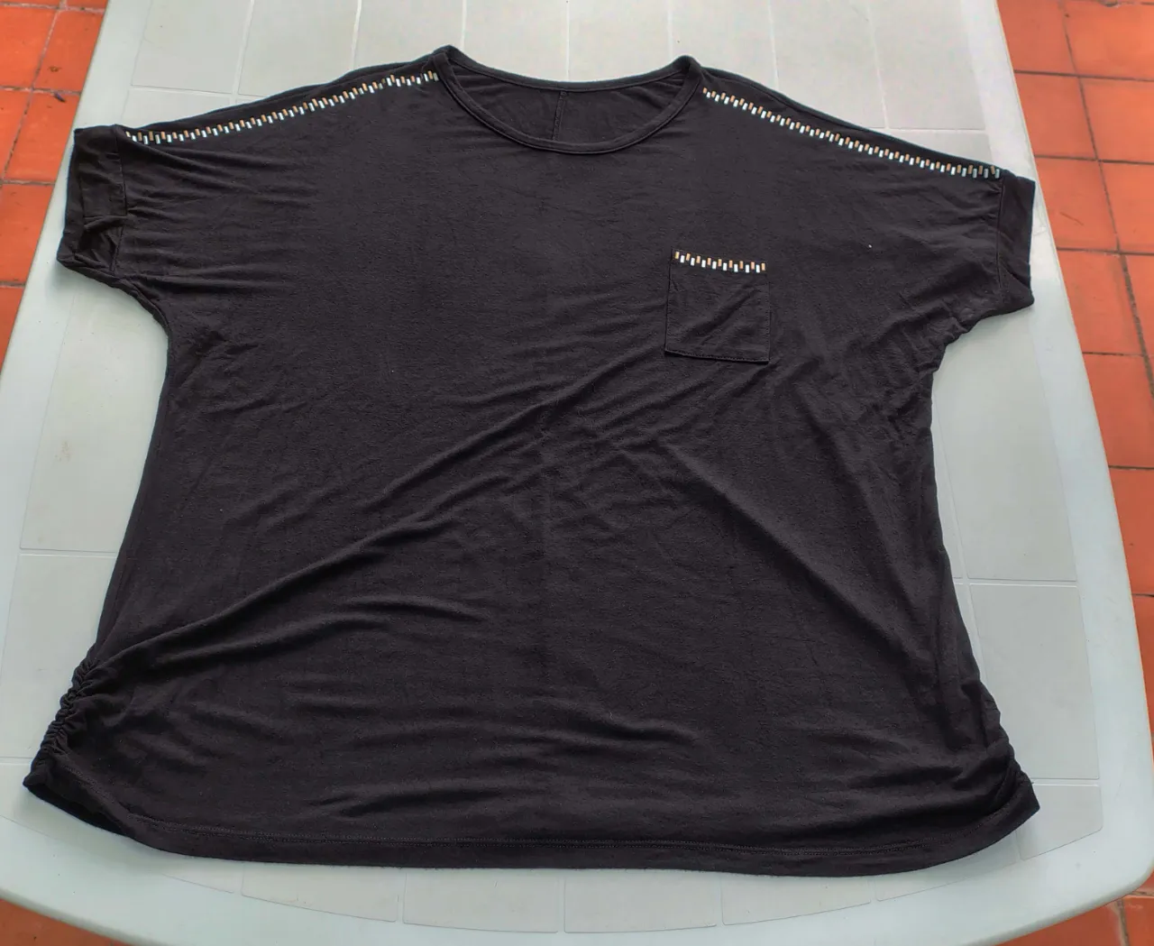 Remera negra de manga corta con detalles de apliques plateados y dorados en los hombros y en el bolsillo. Posee un detalle de fruncido en la cintura de ambos lados.