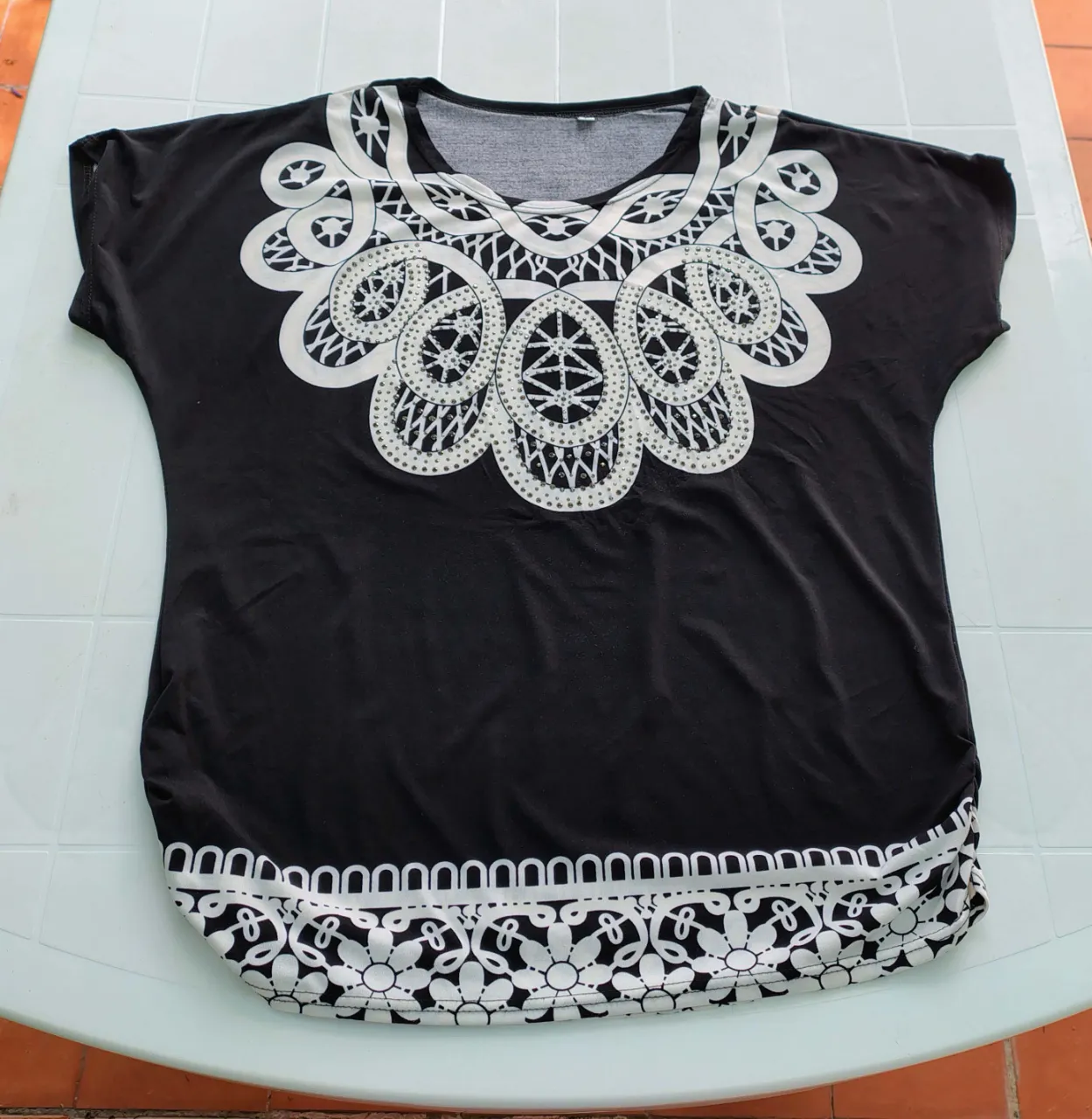 Remera negra con estampa ornamental blanca en el cuello y en el borde inferior. Mangas cortas.