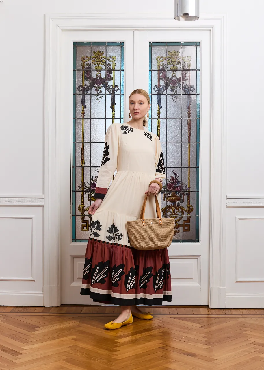 Vestido largo de algodón color crudo con mangas largas y volados. Posee un estampado floral en negro y bordó en la falda y en las mangas. Ideal para un look boho chic.