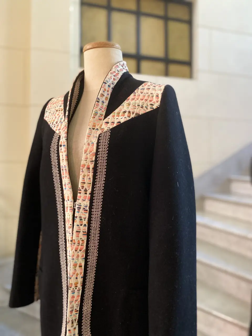 Elegante tapado negro con detalles artesanales en el cuello y solapas. Diseño sofisticado con detalles en tela estampada, ideal para un look de invierno.