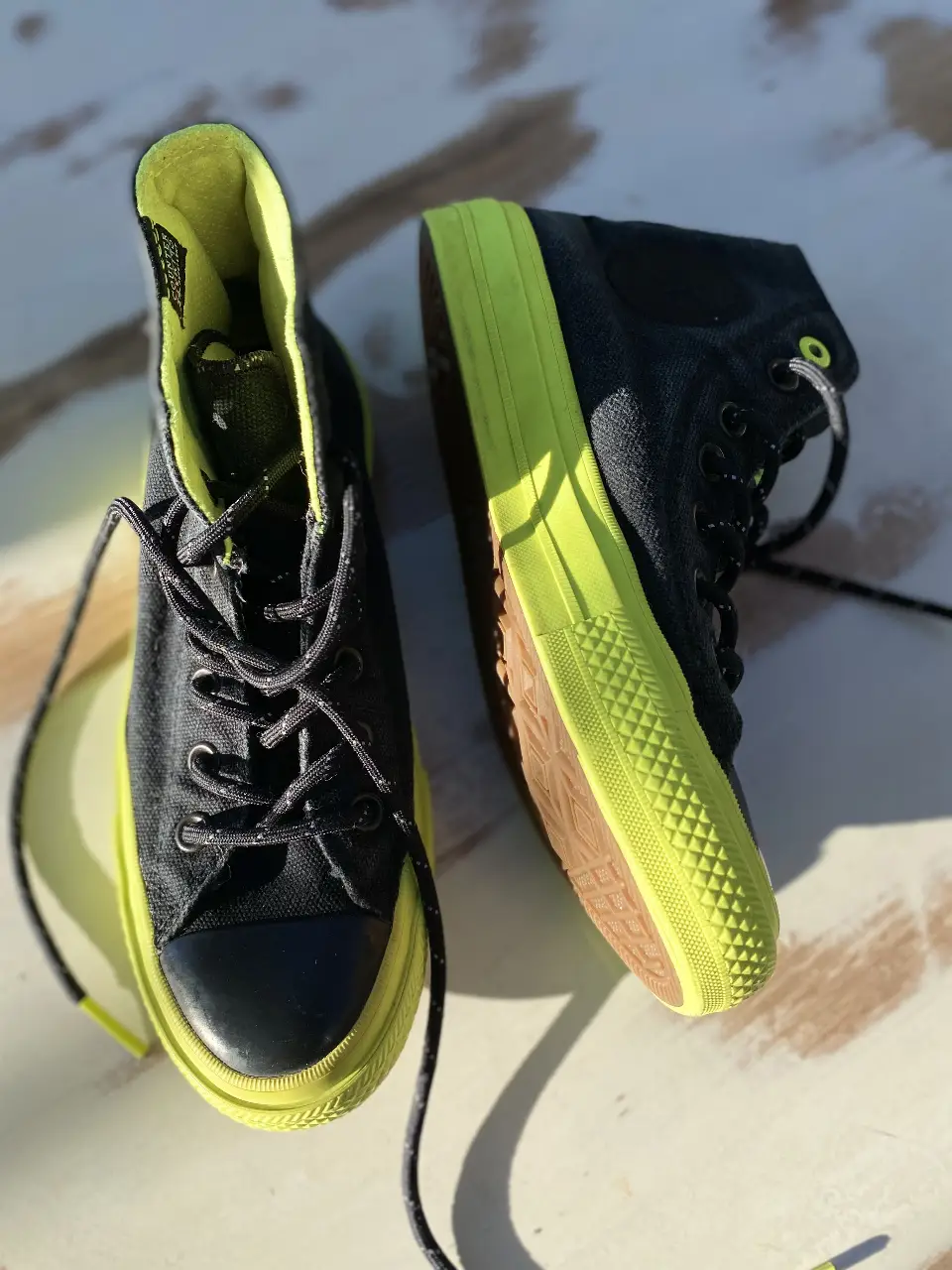 Zapatillas Converse Chuck Taylor All Star de caña alta en color negro con detalles en amarillo flúo. Suela de goma marrón con el logo de la marca. Ideales para un look urbano y moderno.