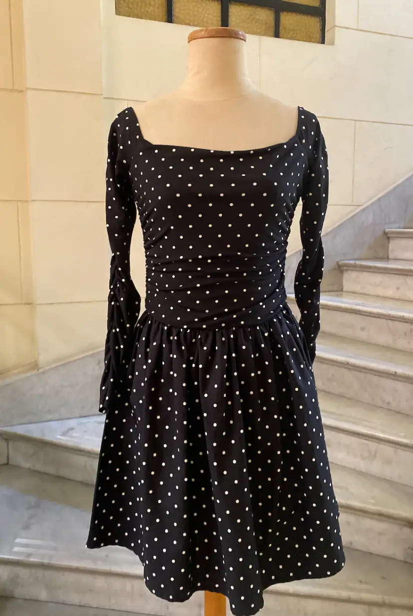 Vestido mini negro con lunares blancos, de manga larga y corte ajustado en la cintura. Ideal para un look vintage y elegante.