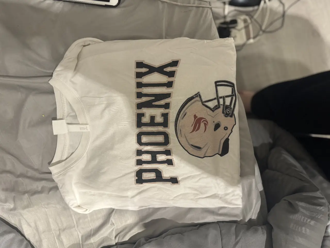 Remera de manga corta blanca con estampado de "Phoenix" y un casco de fútbol americano. Ideal para fanáticos del deporte y un look casual.