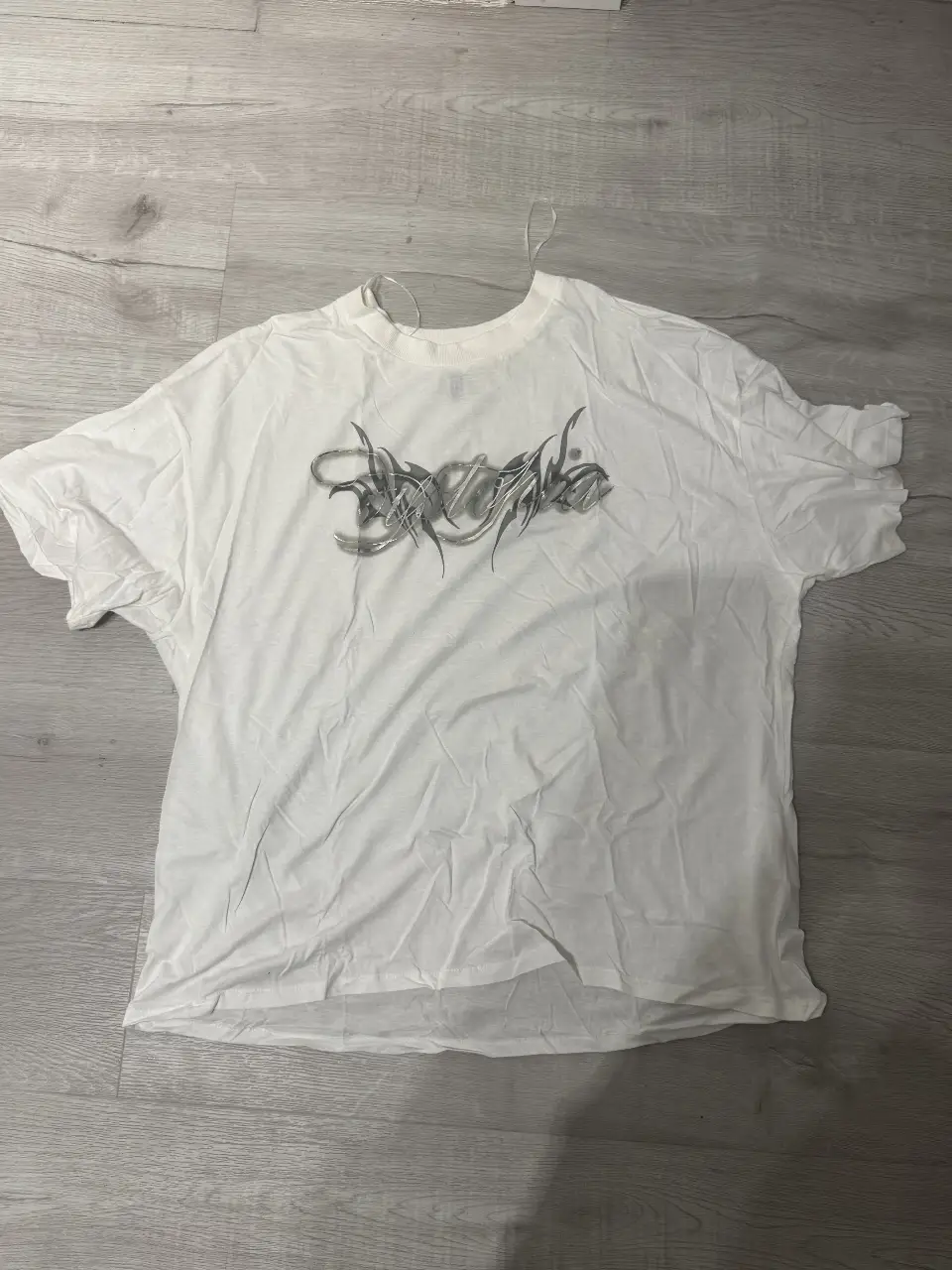 Remera blanca con estampado "Dystopia" en plateado. Corte oversize, ideal para un look urbano y moderno. Perfecta para combinar con jeans o shorts.