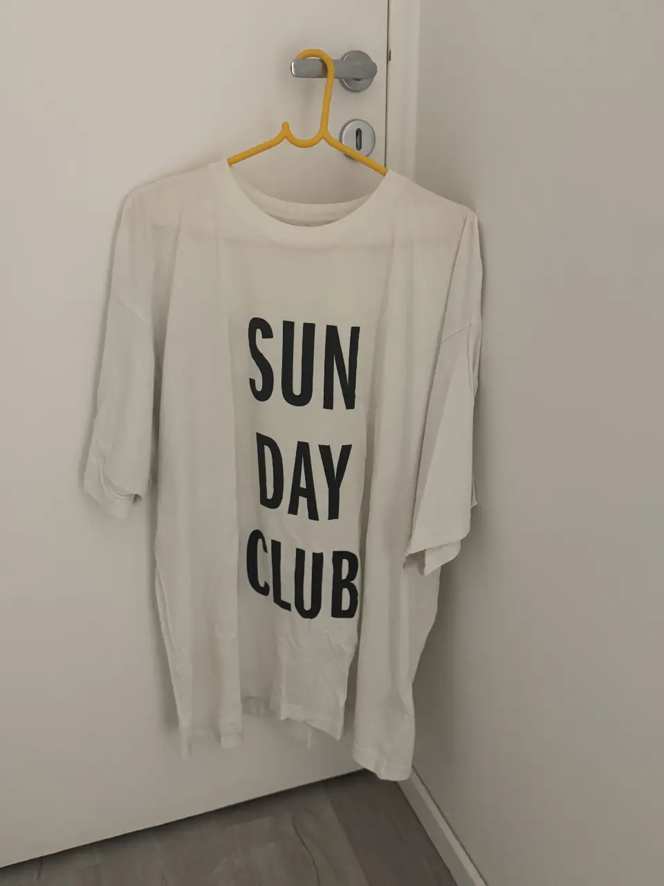 Remera blanca de algodón con estampado "SUNDAY CLUB" en negro. Corte holgado, ideal para un look casual y cómodo.