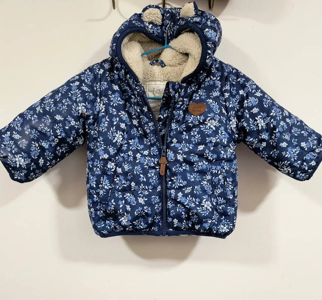 Campera para niña con capucha y orejas, con estampado floral en tonos azules y forro de sherpa. Ideal para el invierno.