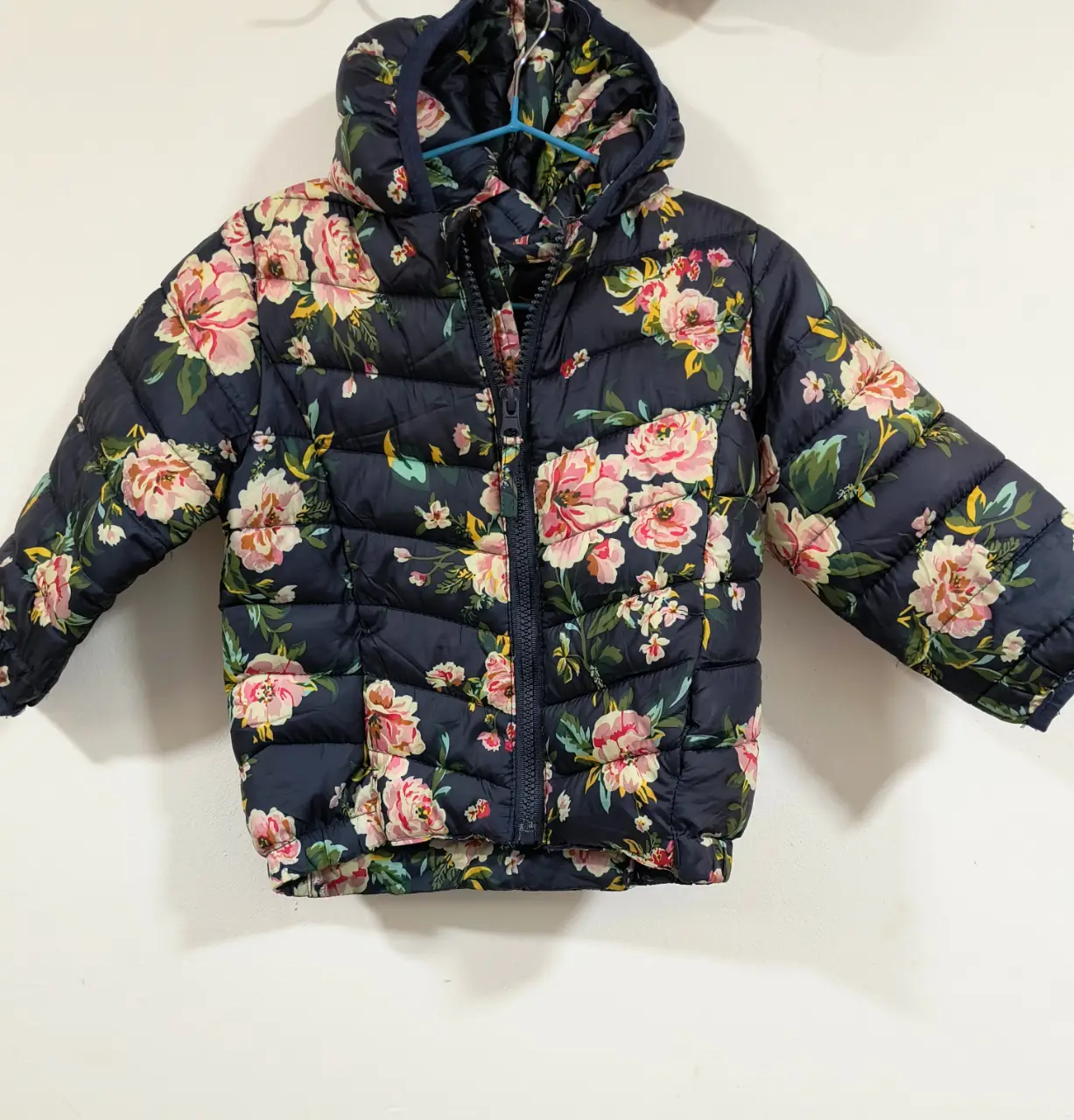 Campera para niña, con estampado floral en tonos rosa y blanco sobre fondo azul marino. Cuenta con capucha y cierre frontal. Ideal para el invierno. Trae la bolsita para guardar.