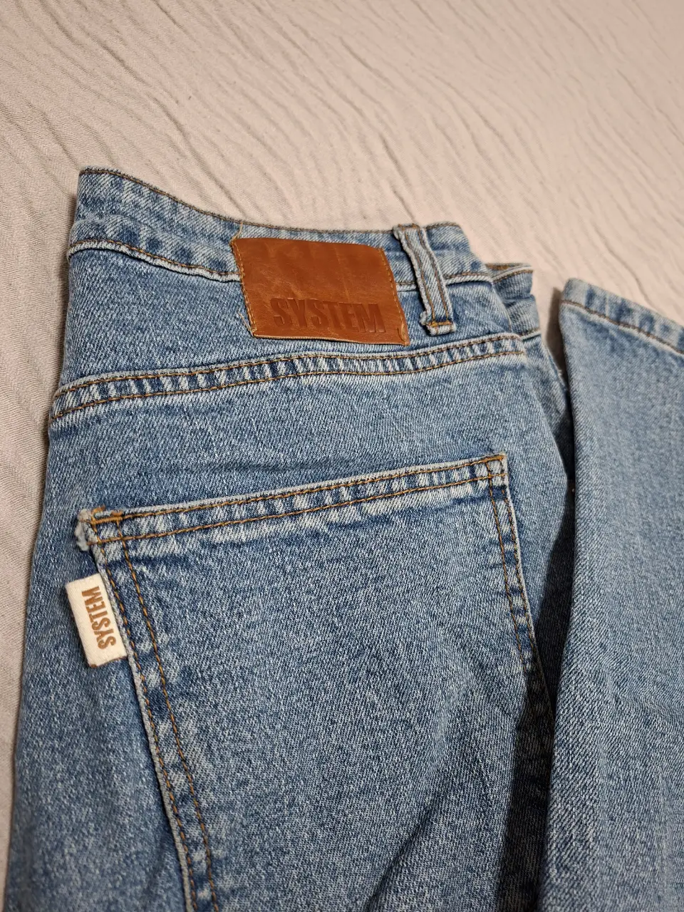 Jeans corte mom, color azul claro, con etiqueta de la marca SYSTEM en el bolsillo trasero y en la parte trasera de la cintura.