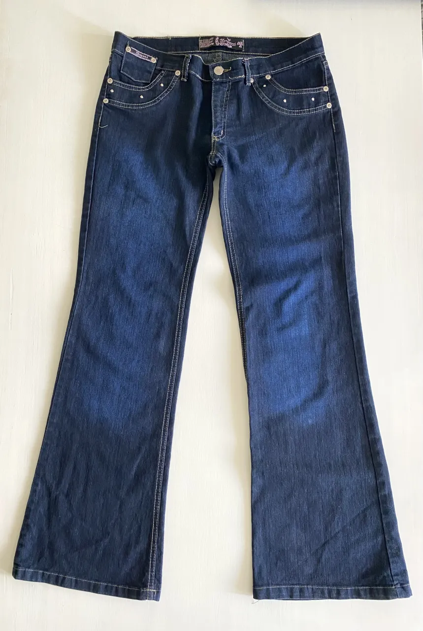 Jeans de corte bootcut con detalles de strass en los bolsillos delanteros y traseros. Costuras blancas visibles y bordado ornamental en los bolsillos traseros. Pantalón Jean Lampassi
Tiro medio. Como nuevo
Talla: 40/42
Largo: 101cm