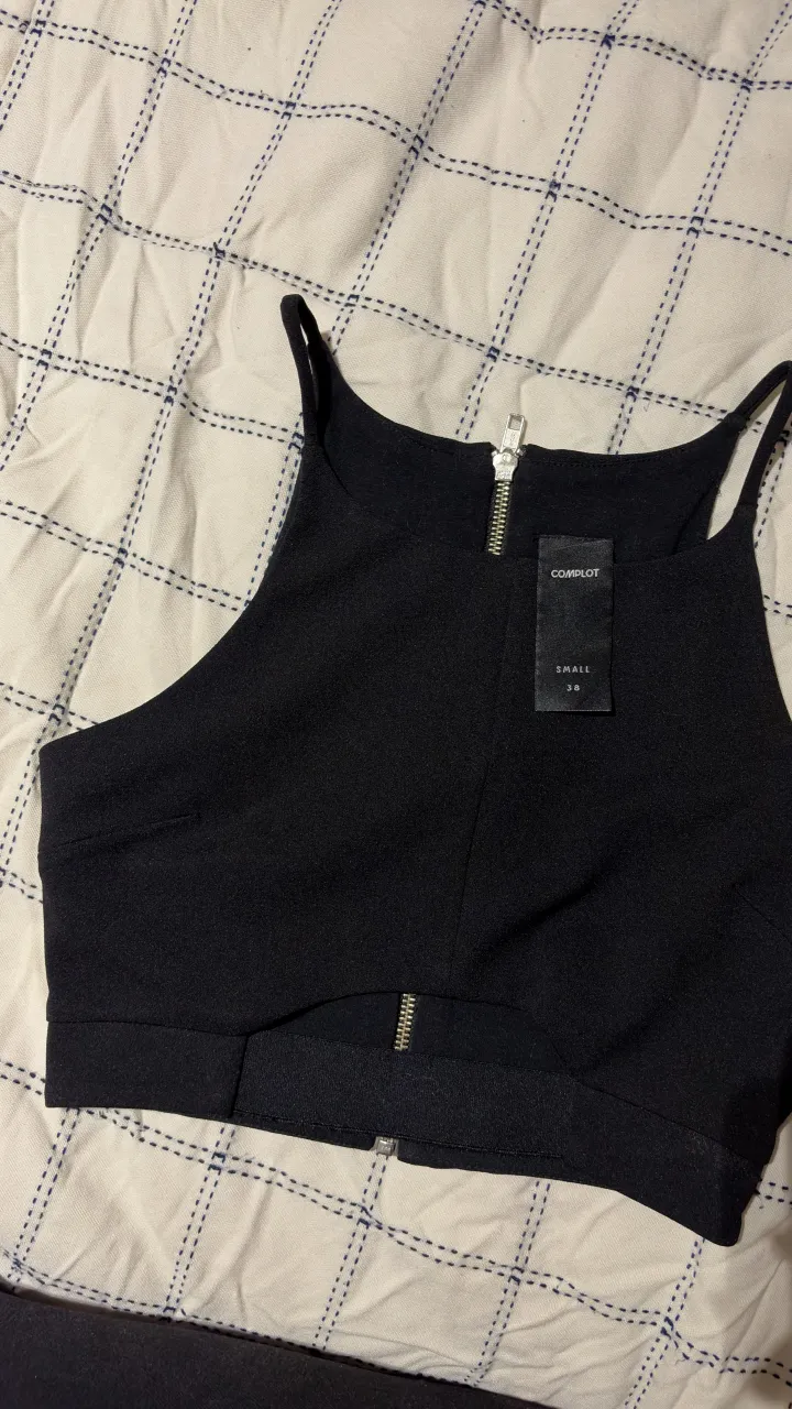 Top negro con cierre metálico al frente. Diseño moderno y versátil, ideal para combinar con jeans o faldas.