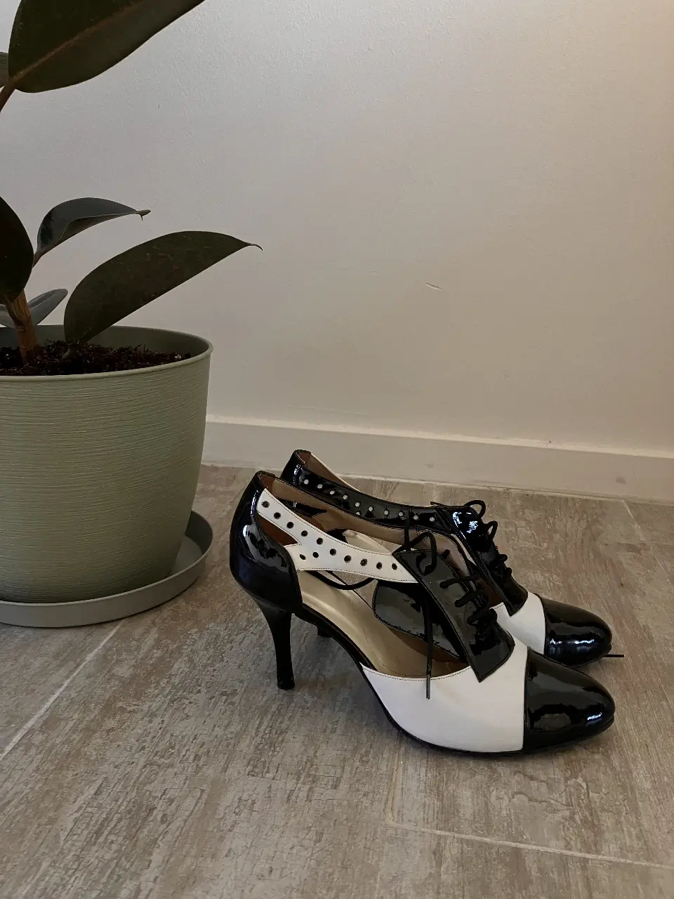 Elegantes zapatos de tacón alto en charol blanco y negro, perfectos para una fiesta o evento formal. Diseño bicolor con detalles de agujeros y cordones.