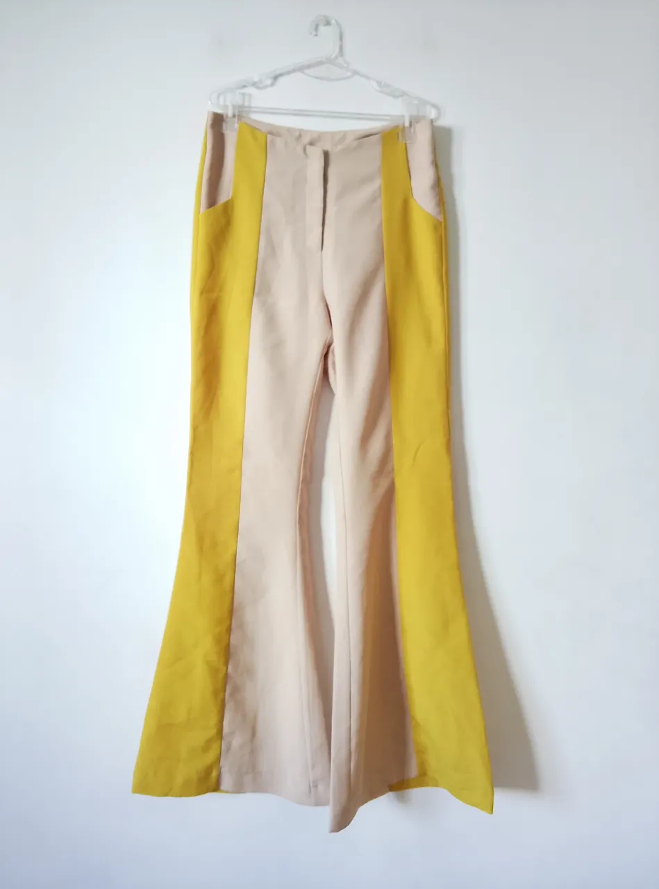 Pantalón sastrero de mujer, con diseño bicolor en beige y amarillo mostaza. Corte campana, tiro alto y cierre con cremallera y botón. Ideal para un look moderno y elegante.