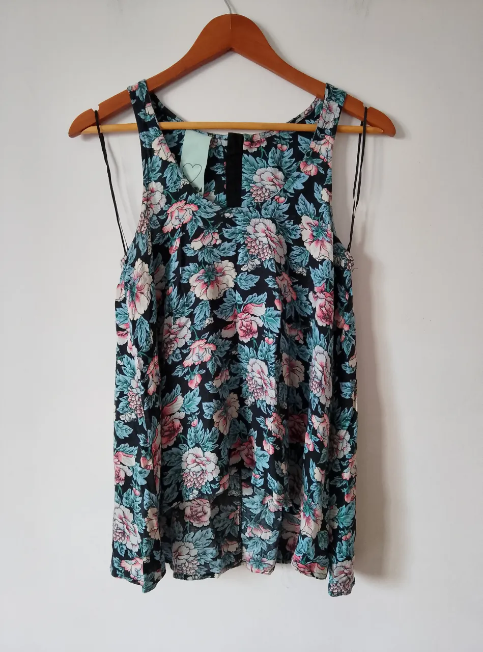 Blusa sin mangas con estampado floral en tonos rosa y celeste sobre fondo negro. Tiene cierre en la espalda y etiqueta con talle.