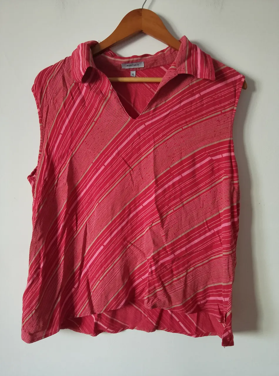 Blusa sin mangas de mujer, con estampado a rayas en tonos rojos y rosados. Cuello en V y detalle de solapa. Ideal para un look fresco y casual.