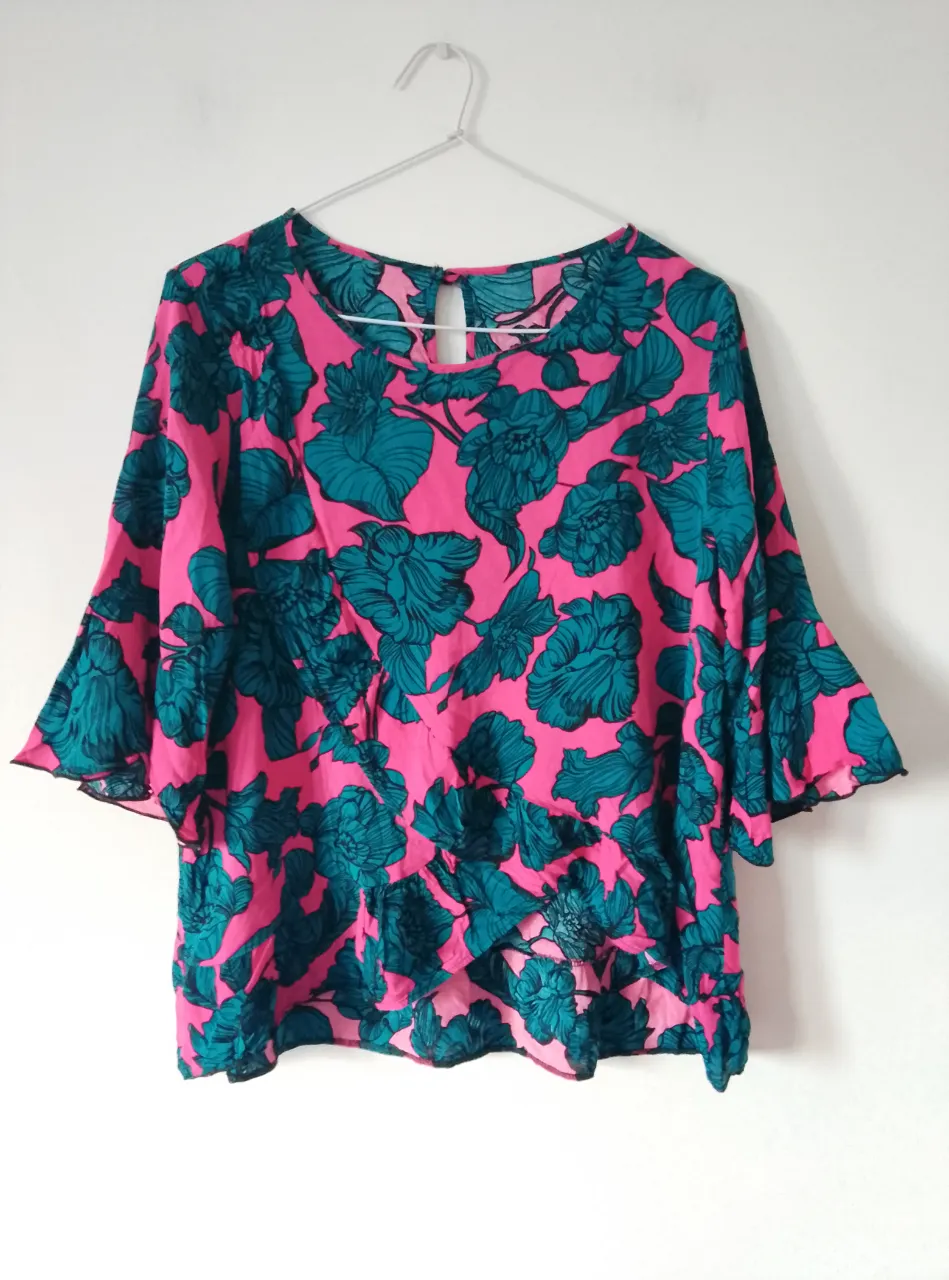 Blusa de mujer con estampado floral en tonos rosa y verdementa oscuro. Diseño con mangas amplias y detalle de volados, ideal para un look fresco y femenino.