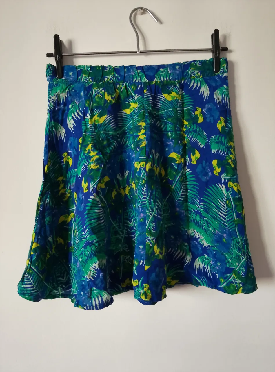 Pollera larga con estampado tropical en tonos azules y verdes, ideal para un look fresco y veraniego. Confeccionada en tela liviana y fluida, perfecta para combinar con tops y sandalias.