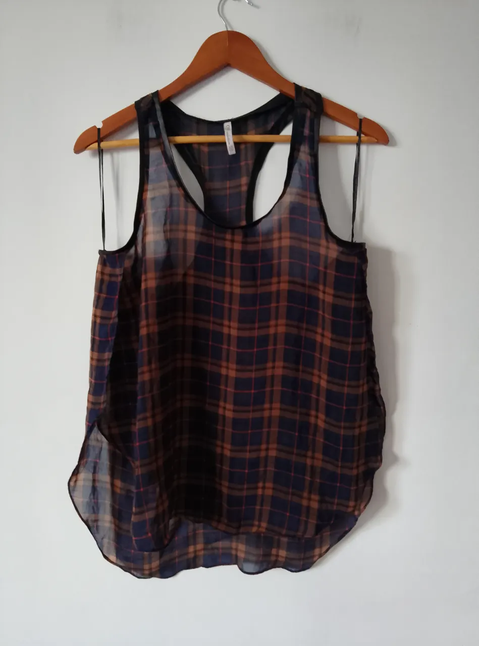 Musculosa transparente de mujer con estampado a cuadros en tonos azul y marrón. Diseño con espalda deportiva y detalles en negro. Ideal para un look casual y fresco.