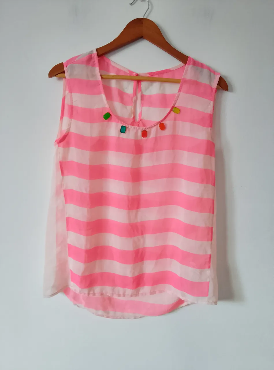 Blusa sin mangas de tela traslúcida a rayas rosas y blancas, con detalles de apliques de colores en el cuello. Ideal para un look fresco y veraniego.