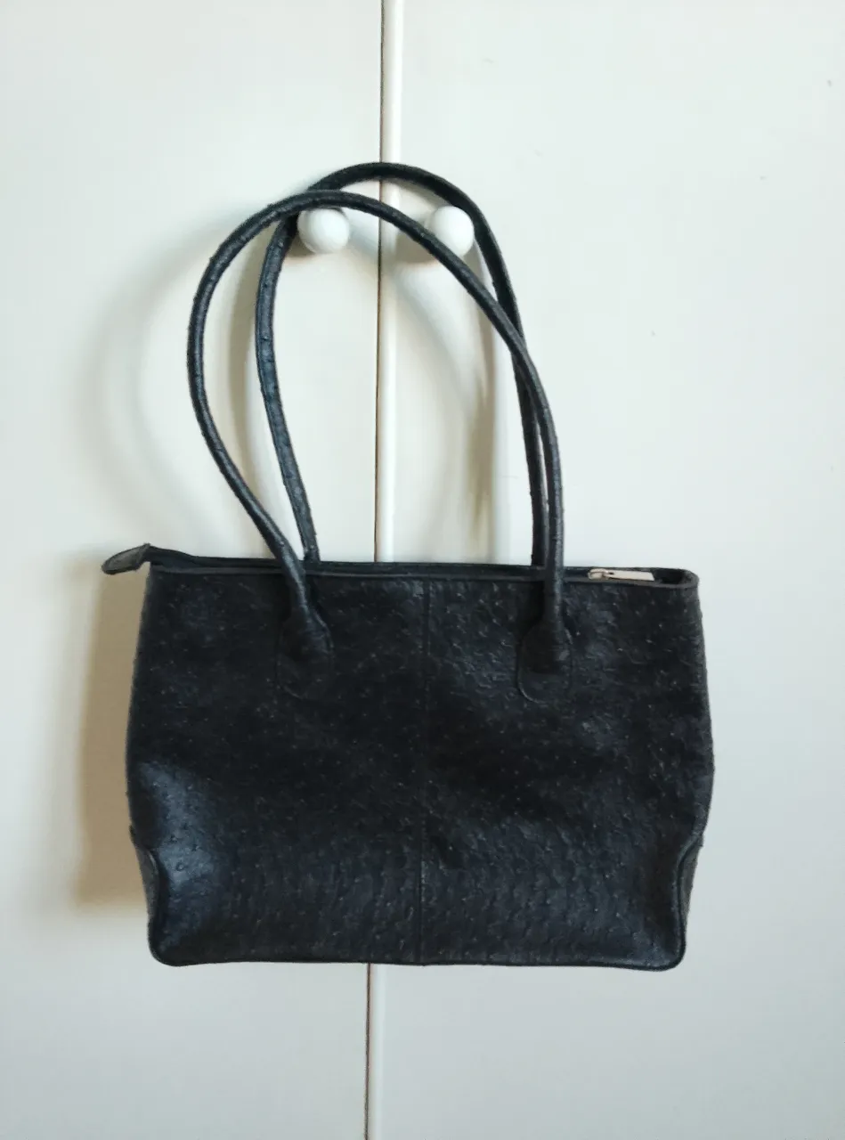 Cartera negra de mano, con textura tipo piel de reptil. Está forrada de poliéster adentro. Posee manijas cortas y cierre superior. Ideal para llevar tus esenciales con estilo.