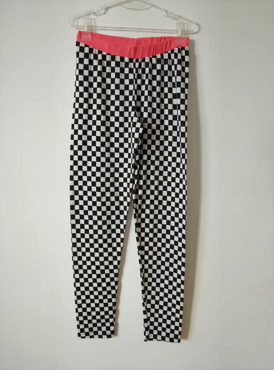 Calzas con estampado de cuadros blanco y negro, cintura elastizada en color coral. Ideal para un look moderno y audaz.