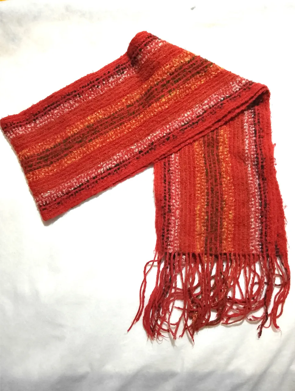 Bufanda tejida a mano en tonos rojos y naranjas, con flecos en los extremos. Ideal para abrigar y darle un toque de color a tus outfits de invierno.