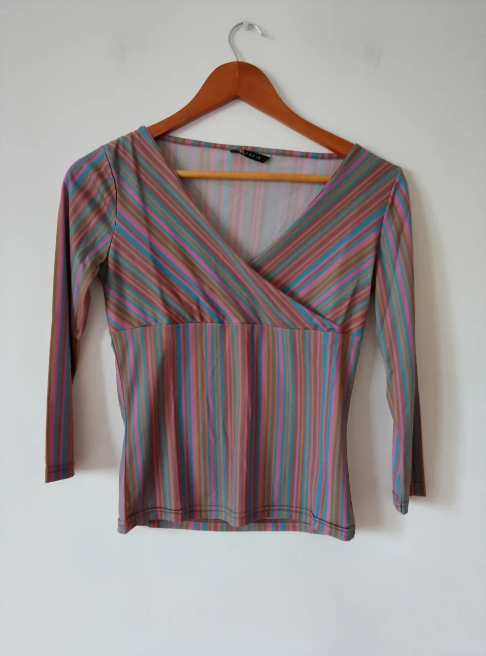 Blusa de manga larga con estampado a rayas en tonos marrones, azules y rosas. Corte cruzado en el frente y cuello en V. Ideal para un look vintage.
