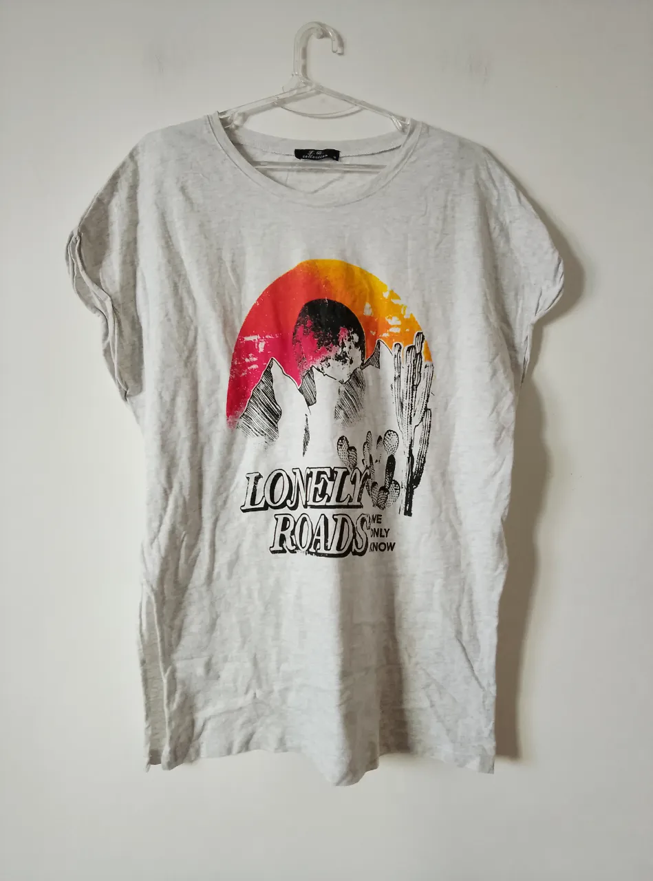 Remera de manga corta gris con estampado de "Lonely Roads" con diseño de montañas, cactus y sol. Ideal para un look casual y relajado.