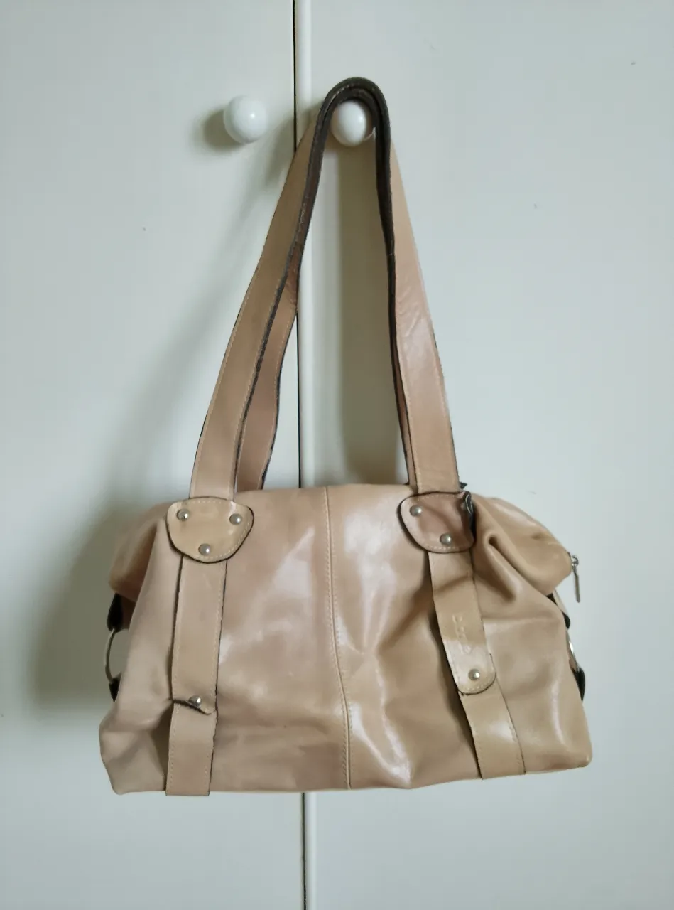 Cartera de hombro de cuero color crudo, con manijas largas y detalles metálicos. Ideal para llevar tus esenciales con estilo. Forrada en el interior de algodón y poliéster con un compartimiento