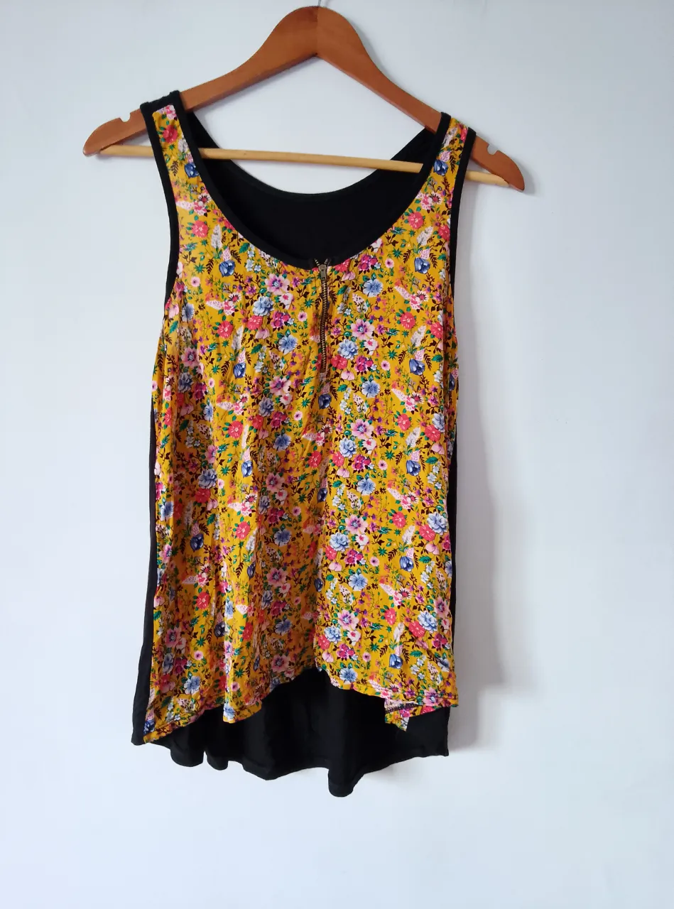 Musculosa de mujer con estampado floral en tonos amarillos, azules y rosas. Tiene un cierre frontal y un diseño de doble capa, con una base negra. Ideal para un look fresco y primaveral.