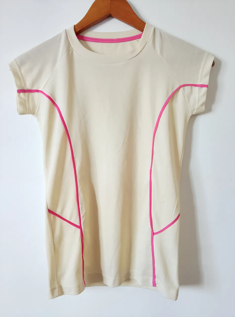 Remera deportiva de color crudo con detalles en rosa. Ideal para actividades físicas.