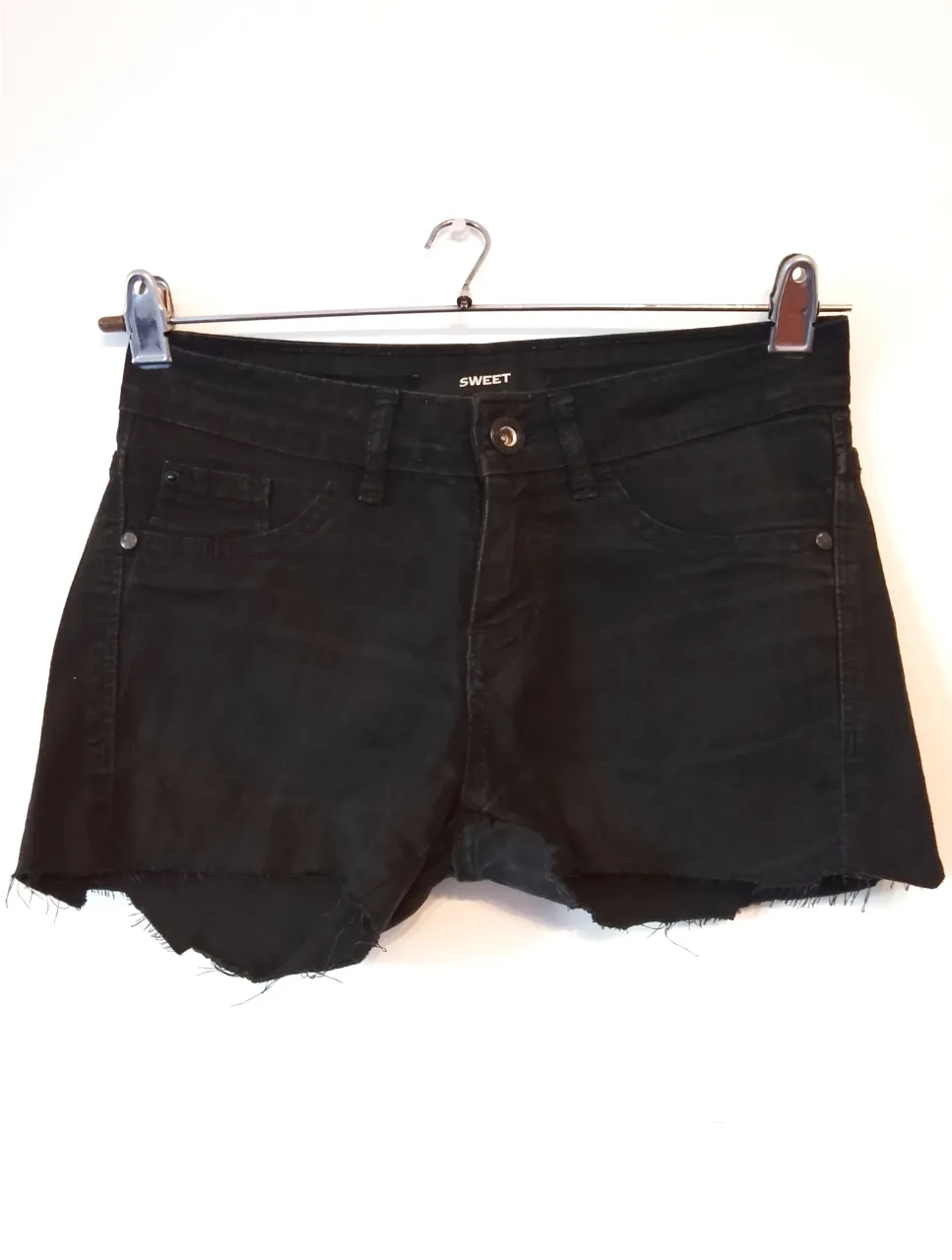 Short de jean negro de la marca Sweet, con corte desflecado en el borde inferior. Ideal para un look casual y moderno.