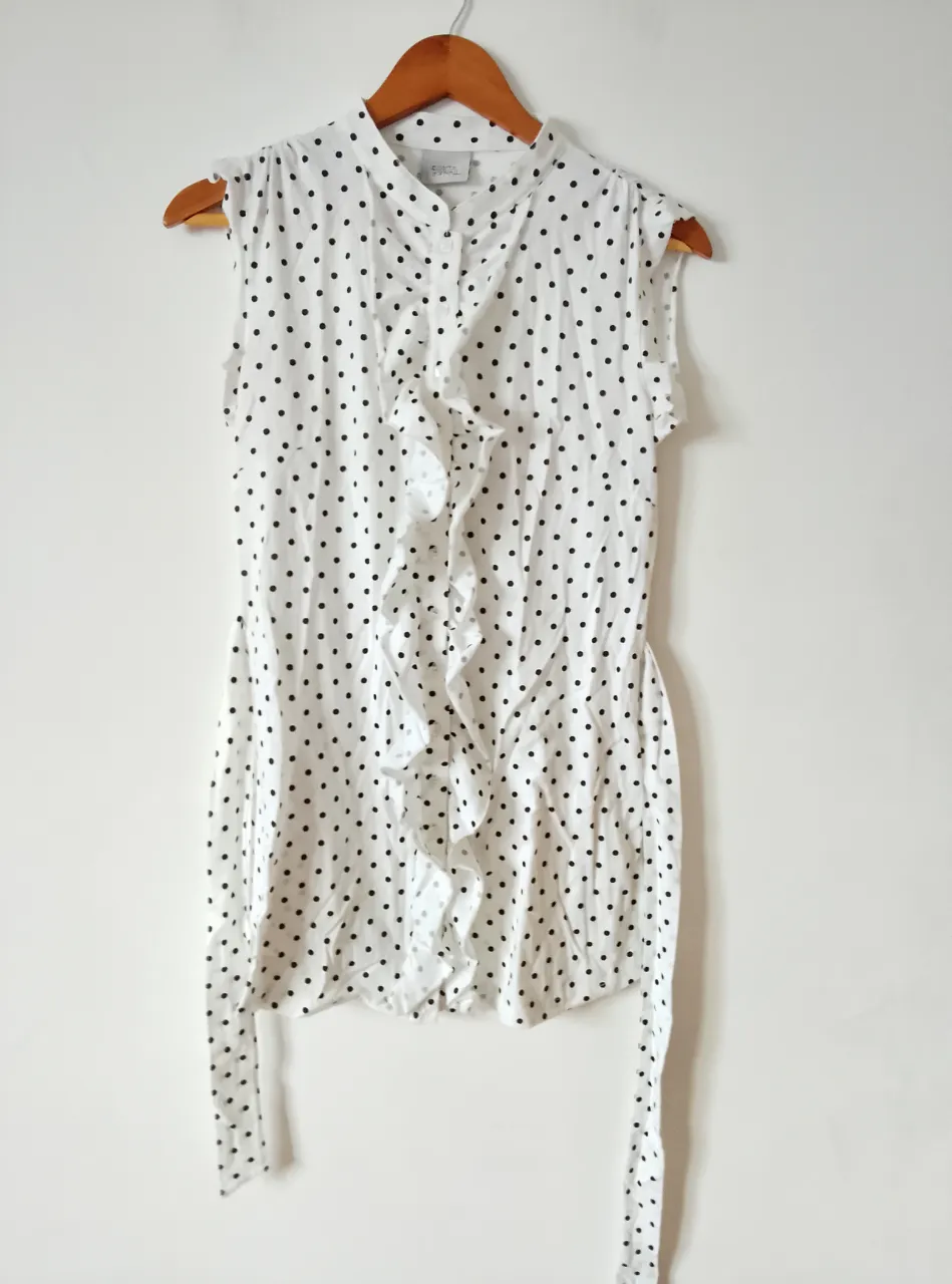 Blusa blanca con lunares negros, sin mangas y detalle de volados en el frente. Ideal para un look casual y fresco.