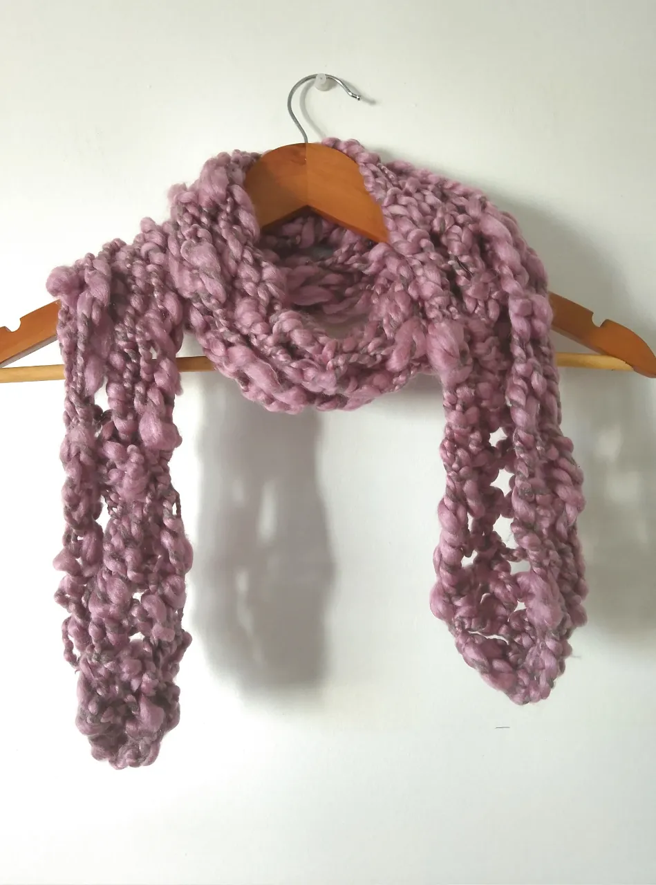 Bufanda tejida a mano en color rosa oscuro, con textura abultada y diseño calado. Ideal para abrigar y complementar cualquier look de invierno.