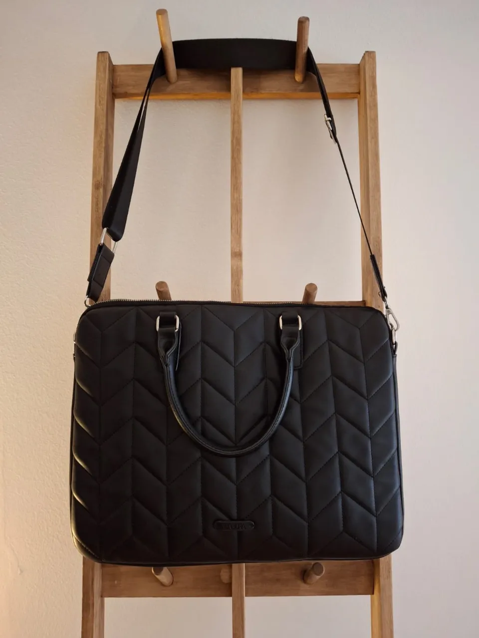 Cartera portanotebook ISADORA negra con diseño acolchado en forma de zigzag. Ideal para llevar tu laptop y otros esenciales con estilo. Cuenta con manijas y correa ajustable para llevar al hombro.