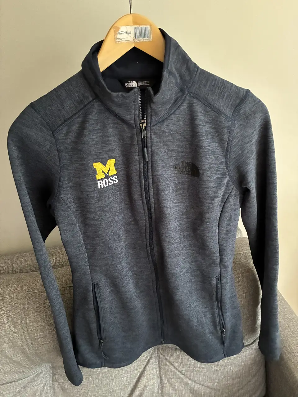 Buzo con cierre The North Face gris oscuro con logo de la Universidad de Michigan. Ideal para uso diario y actividades deportivas.