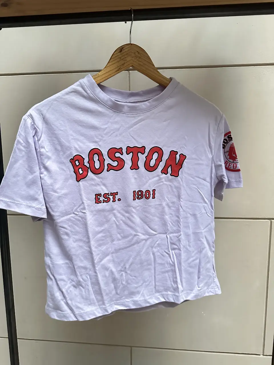 Remera de algodón blanca con estampado "BOSTON" en rojo y el logo de los Red Sox en la manga. Ideal para fanáticos del béisbol y un look casual. color lila talle único 