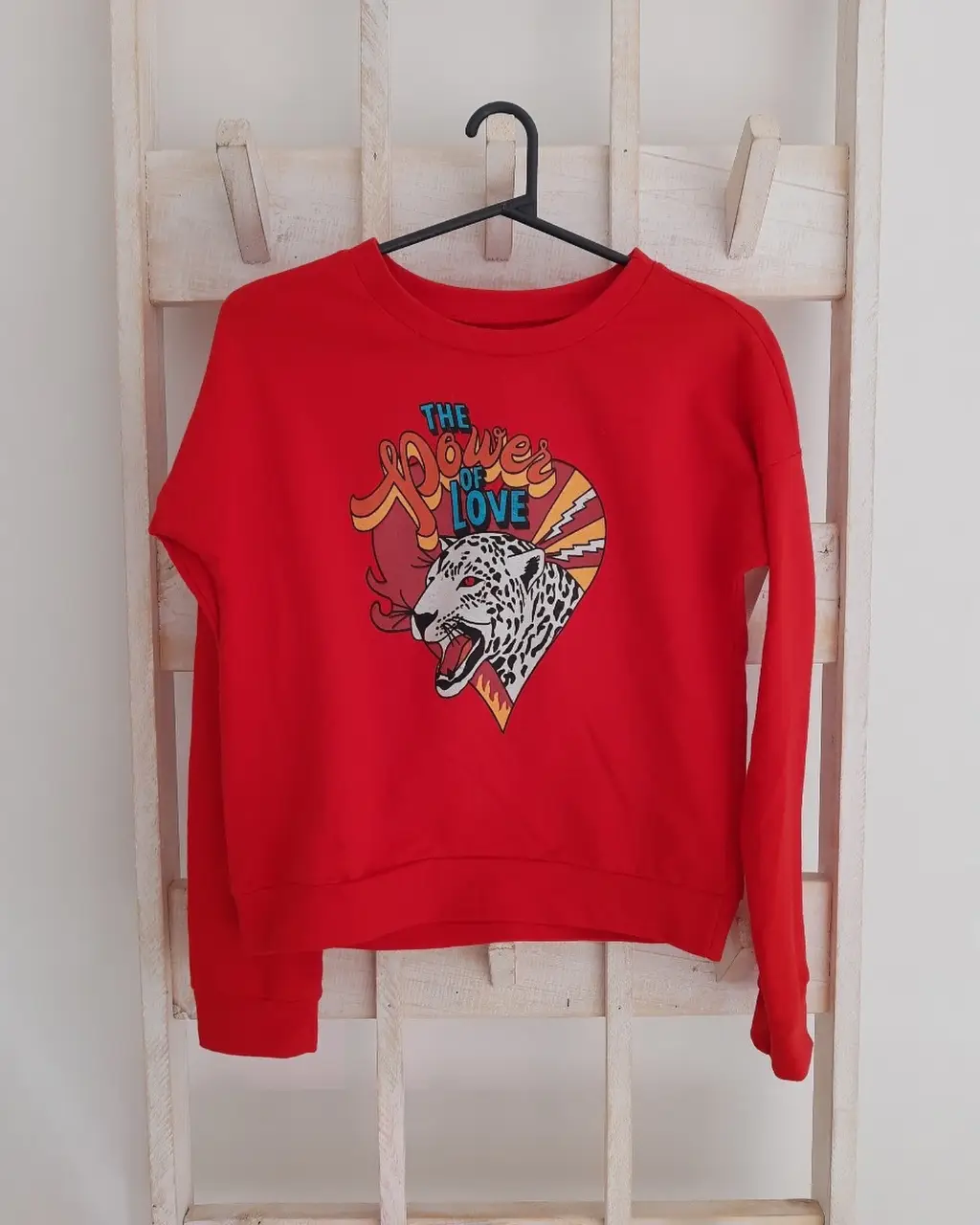 Buzo de cuello redondo rojo con estampado "The Power of Love" con un diseño de un leopardo y detalles en amarillo y celeste. Ideal para un look casual y con onda. Talle unico