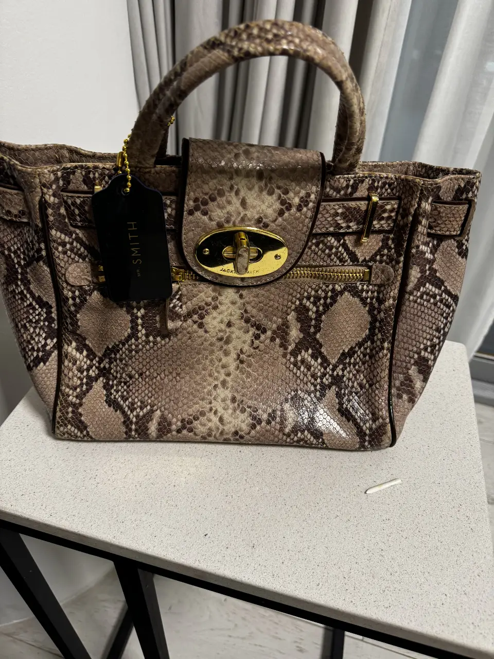 Cartera de mano Jack Smith con estampado de serpiente. Ideal para un look sofisticado y moderno. Detalles dorados y cierre con solapa.