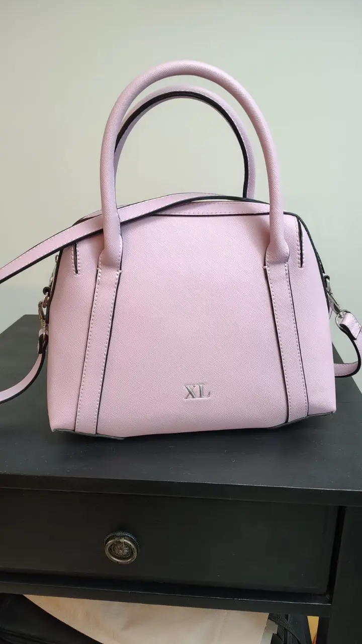 Cartera de mano rosa claro con detalles en negro. Ideal para llevar tus esenciales con estilo. Cuenta con manijas cortas y una correa larga desmontable. Interior espacioso con bolsillo interno con cierre.