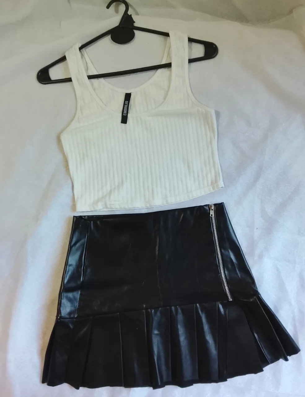 Conjunto de top blanco acanalado y pollera negra de cuero sintético con tabla y cierre.