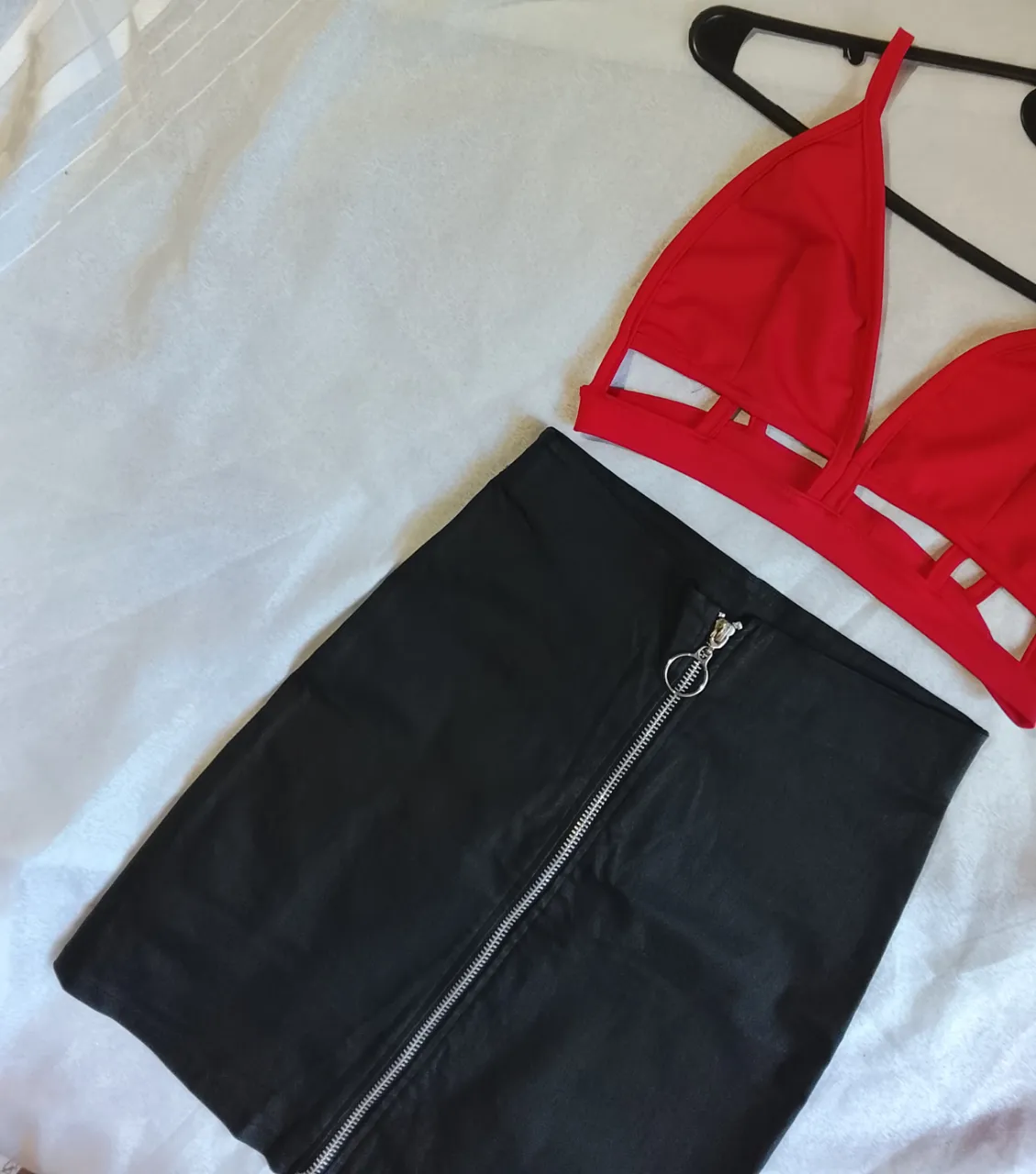 Conjunto de dos piezas: corpiño rojo con recortes y falda negra con cierre metálico y aro.