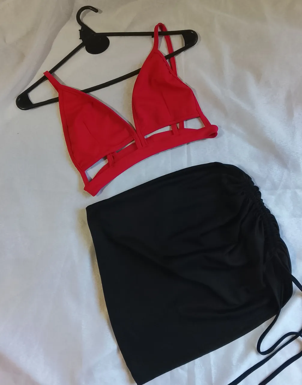Conjunto de bikini rojo y negro. El corpiño es rojo, con tiras finas y recortes en la parte inferior. La bombacha es negra, con fruncido y cordones a los costados.