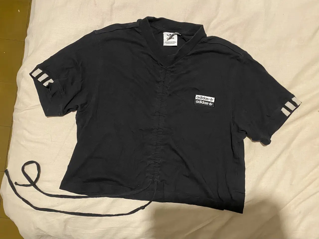 Remera Adidas negra con detalles blancos. Diseño con fruncido en el frente y las clásicas tres tiras en las mangas, tiene tiras ajustables 