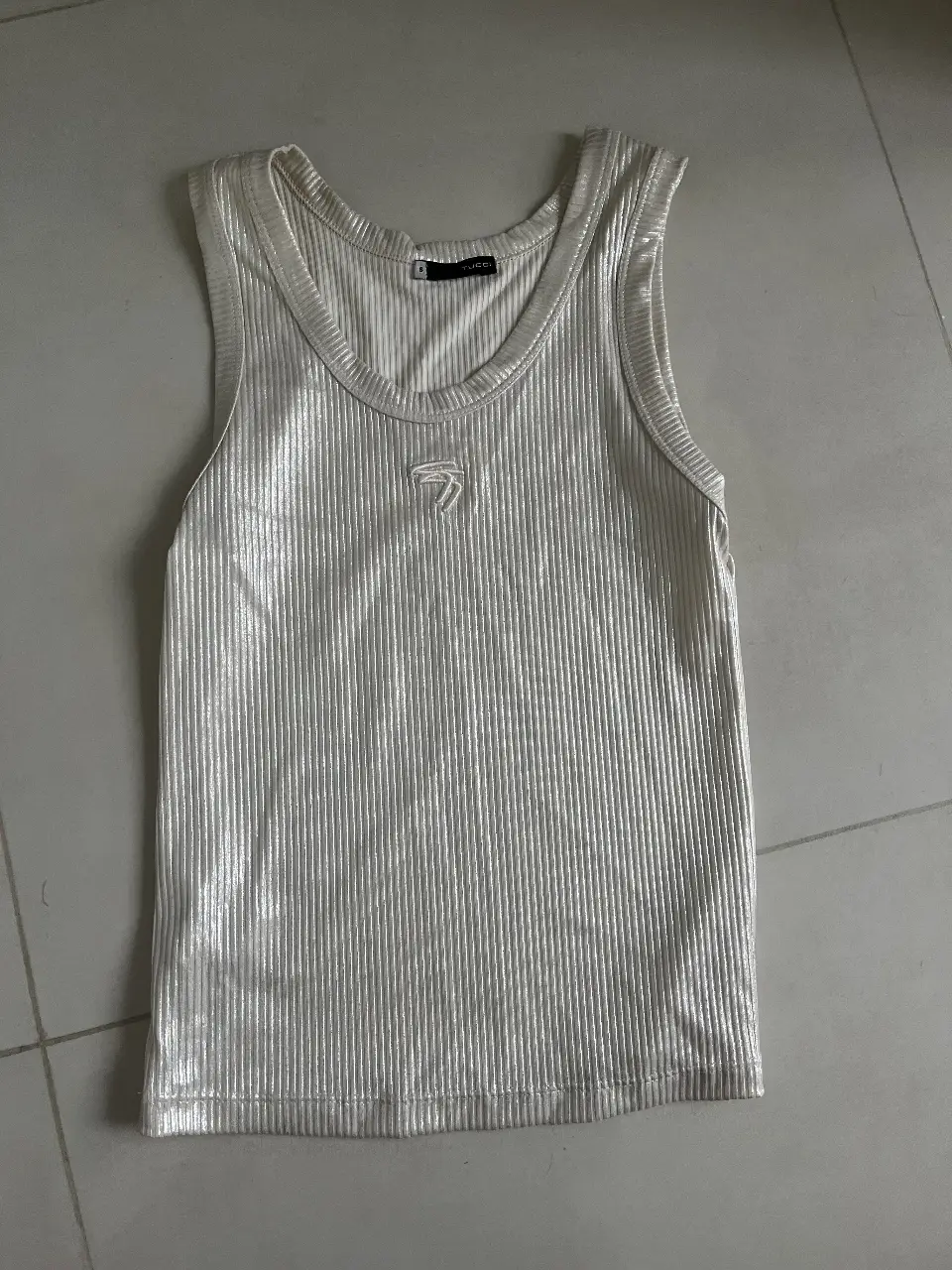 Musculosa de mujer, de color blanco, con diseño acanalado y detalle de logo bordado. Ideal para un look casual y moderno.