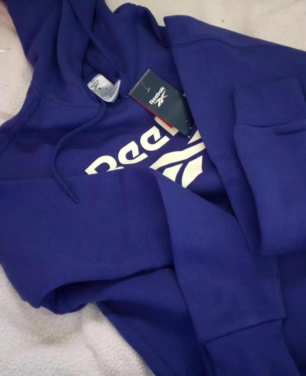 Buzo canguro de hombre/mujer Reebok, color azul con logo blanco. Ideal para un look deportivo y casual. Confeccionado en tela suave y cómoda, perfecto para el día a día.