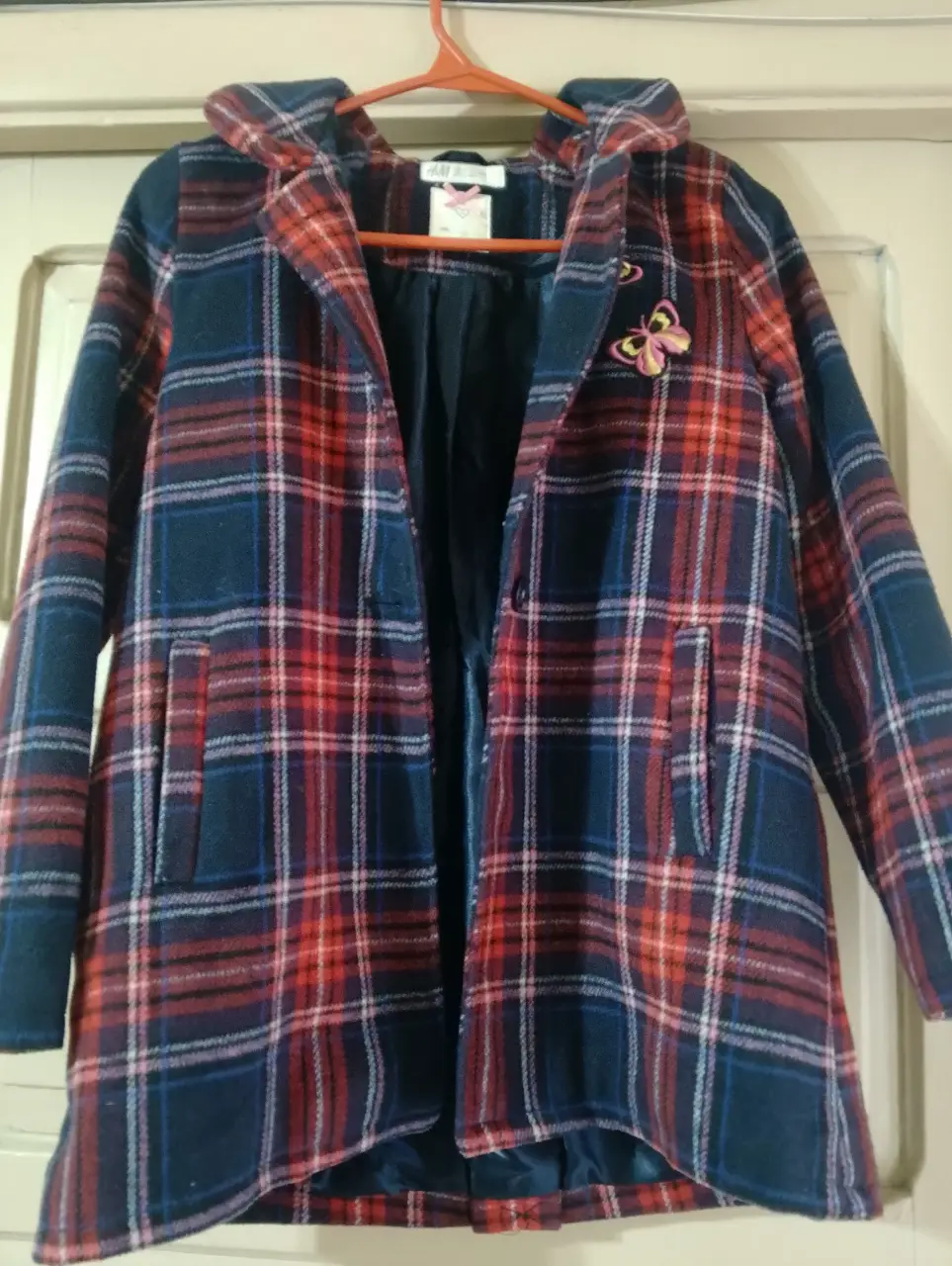Campera de abrigo con capucha, diseño a cuadros en tonos azul y rojo. Posee un detalle de mariposa bordada y bolsillos delanteros. Ideal para el invierno.
