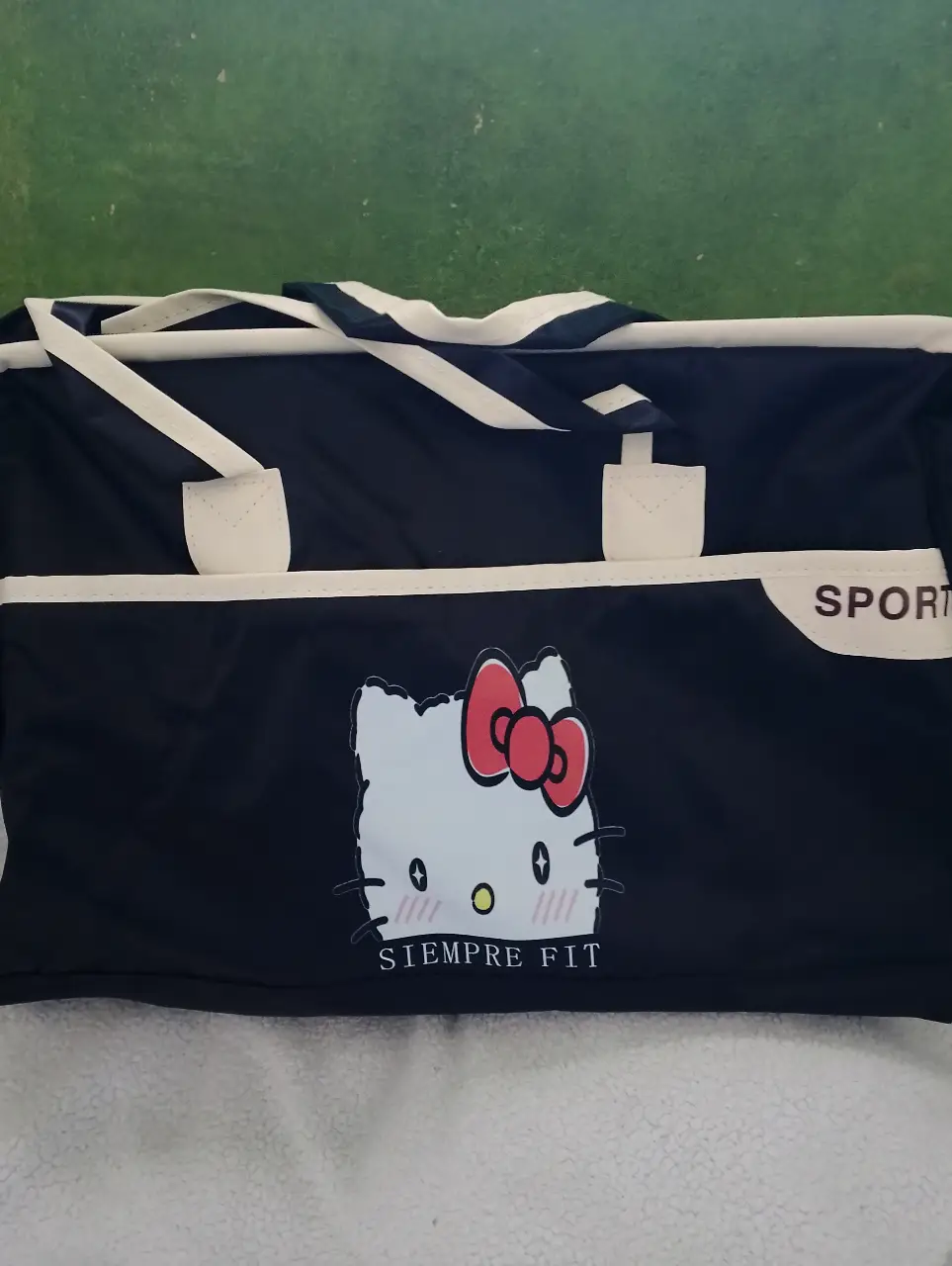 Bolso deportivo negro con diseño de Hello Kitty y detalles en blanco. Ideal para llevar al gimnasio o para viajes cortos. Cuenta con un bolsillo exterior y asas para llevarlo cómodamente. 47 cm de ancho y 32 cm de alto. 3 bolsillos exteriores.